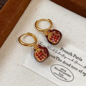 Detail of gold-plated hoop earrings with red zircon pomegranate pendants and enamel