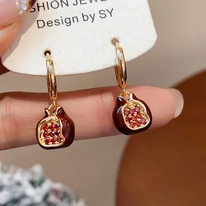Macro detail of gold-plated pomegranate hoop earrings with red zircon and enamel