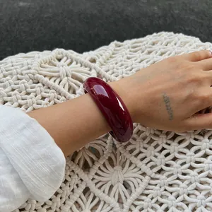 Close-up of a deep burgundy resin open bangle worn on a wrist over woven texture.