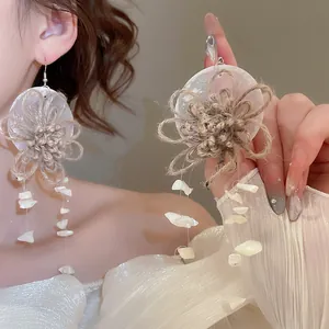 Close-up view of bohemian straw flower earrings featuring iridescent shell dangles.