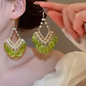 Detail view of bohemian large green sequin dangle earrings with white pearls on model