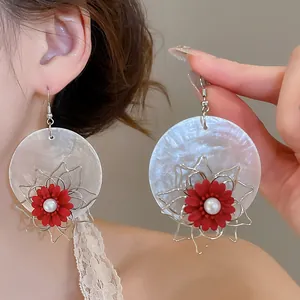 Close-up of exaggerated red flower earrings with pearlescent disc on a model
