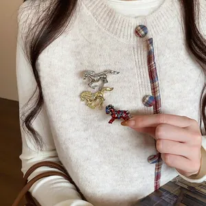 Detail shot of three elegant rhinestone horse brooches pinned on a white cardigan.