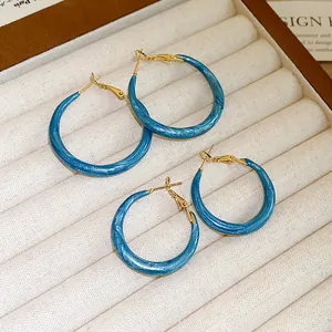Macro detail showing texture of blue marbled enamel hoop earrings on velvet jewelry tray