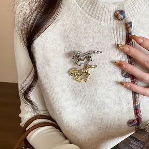 Detailed view of gold and silver horse brooches with crystal accents on a white knit