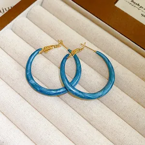 Close-up detail of blue marbled enamel hoop earrings with gold-tone hardware
