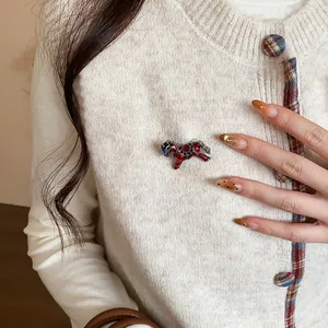 Detailed view of a small red enamel horse brooch with rhinestones on a white sweater.