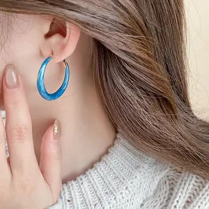 Detail of blue enamel hoop earring with marble effect worn by a model.
