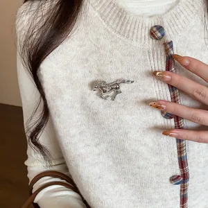 Detailed view of a silver horse brooch with rhinestones pinned on a cream cardigan.