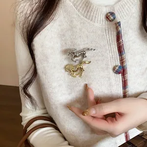 Close-up of two elegant horse-shaped brooches with rhinestones on a white cardigan.