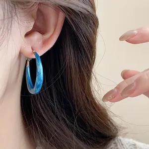 Detailed close-up showing a blue marbled oil-drop hoop earring on the model's ear
