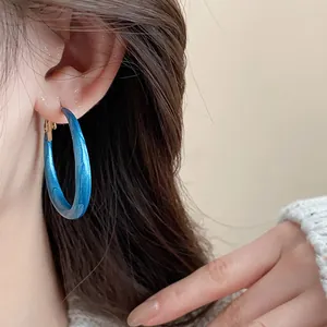 Close-up detail showing blue marble oil-drop hoop earrings worn by an Asian model