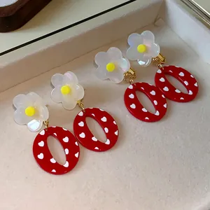 Primer plano de pendientes de resina con flores blancas y corazones rojos en un joyero.