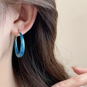 Macro detail of blue oil-dripped marbled hoop earring with retro aesthetic on model