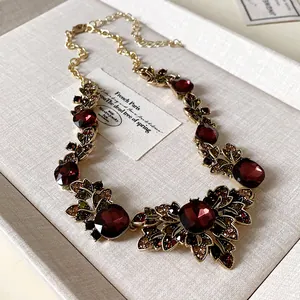 Vue détaillée d'un collier vintage avec pierres bordeaux et motifs de feuilles dorées élégant
