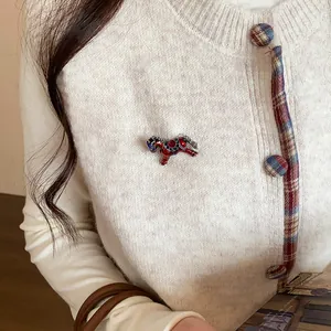 Detail of a red rhinestone horse brooch pinned on a cream knit cardigan accessory