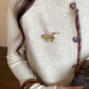 Detailed view of a gold small horse brooch with crystal rhinestones on a white knit sweater