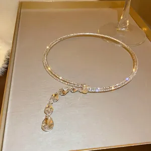 Close-up of zircon water drop choker necklace on a gold tray with a wine glass