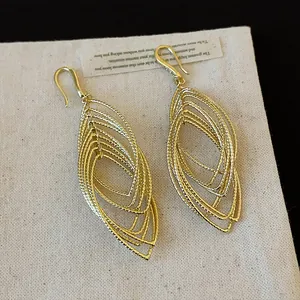 Detailed macro shot of elegant gold-layered oval dangle earrings with textured hollow design.