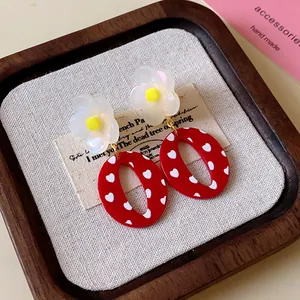 Detalle en primer plano de pendientes de resina roja con corazones blancos y flor perlada