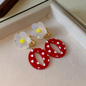 Vista detallada de los pendientes de clip de resina roja con flor y corazones blancos