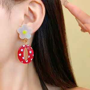 Detalle de pendientes ovalados de resina roja con corazones blancos y flor blanca