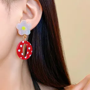 Primer plano de pendientes de resina roja con flores y corazones de estilo vintage en la oreja