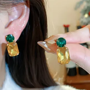 Close-up detail of square stud earrings with emerald green and champagne stones