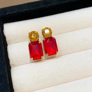 Close-up of elegant silver needle earrings with round yellow and rectangular red gems.