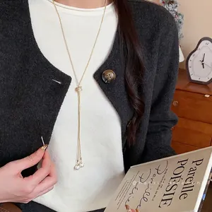 Elegant gold Y-necklace with pearls worn over a white sweater and dark cardigan