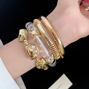Close-up of stacked metal and acrylic geometric bracelets with a vintage gold finish