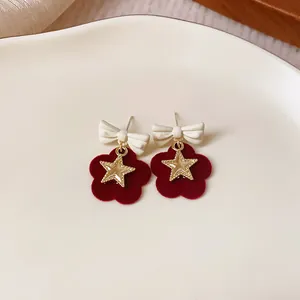 Close-up of elegant red flocked flower earrings with white bows and gold stars for winter.