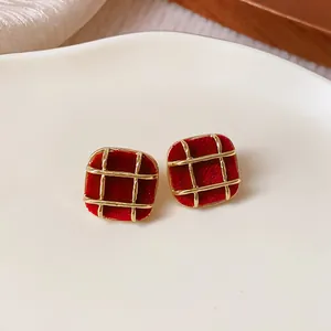 Close-up of red flocked square earrings with gold grid overlay on a white plate