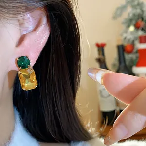 Elegant close-up of rectangular amber and green gemstone earrings on a female model