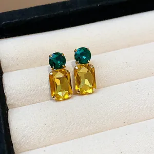 Detailed view of square yellow crystal stud earrings with green stones on velvet tray