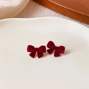 Close-up of elegant red velvet bow stud earrings with silver needles on a ceramic dish