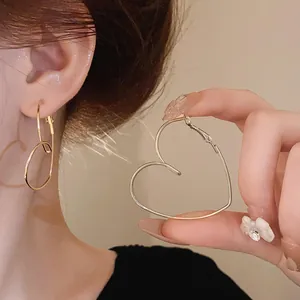 Vue détaillée de boucles d'oreilles créoles cœur évidé dorées portées par un mannequin.