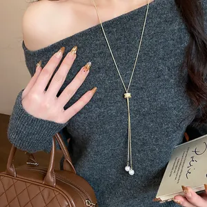 Minimalist gold necklace with zircon slider and pearls worn on a grey sweater