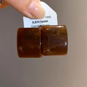 Λεπτομέρεια από τετράγωνα σκουλαρίκια από μάρμαρο ρητίνης σε καφέ και χρυσό μοτίβο.
