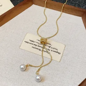 Close-up of elegant gold snake chain necklace with twin pearl pendants on a vintage card.