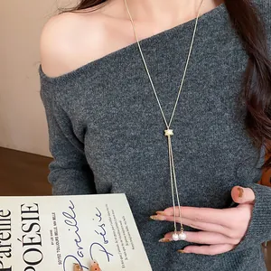 Detail view of a minimalist long gold necklace with zircon and pearls worn on a grey sweater