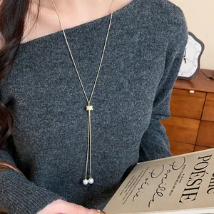 Close-up of a elegant Y-shaped gold pearl sweater necklace on a grey knit top