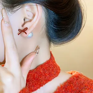 Macro view of a stylish red bow and pearl stud earring elegantly worn on a female ear.