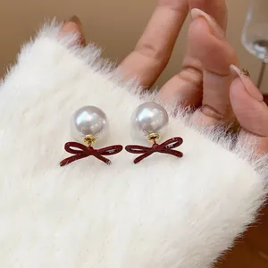 Close-up view of elegant burgundy enamel bow-knot and large white pearl stud earrings