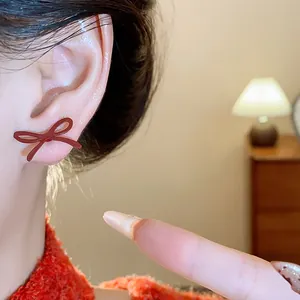Close-up of a vintage red ribbon bow earring worn on ear with soft warm lighting