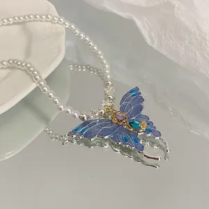 Detail view of an elegant butterfly pendant necklace featuring blue enamel and white pearls