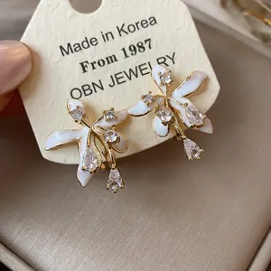 Detailed view of white floral stud earrings with cubic zirconia and gold plating on a card.