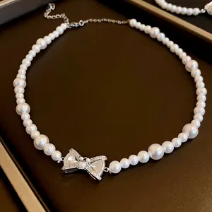 Close-up detail of a silver-toned rhinestone bow pendant on a lustrous white pearl necklace (95 chars)