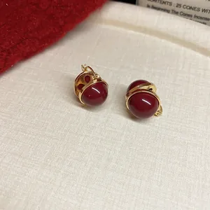 Close-up of retro Ancora red round stud earrings with gold-toned metal wrap.