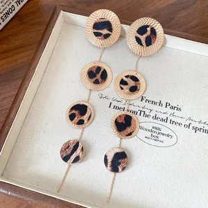 Détail de boucles d'oreilles pendantes rondes léopard avec bords dorés texturés.